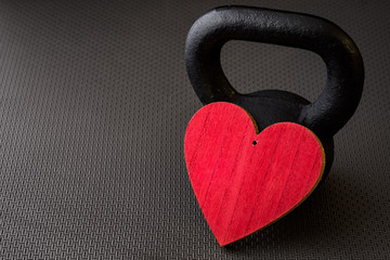 Black kettlebell on a black gym floor with large red heart to celebrate Valentine’s Day fitness