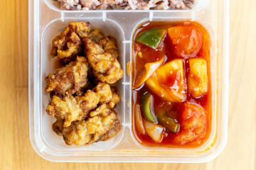 Top view of Thai styled organic Sweet and Sour fried with pork and rice berry in food grade box with wooden background. 