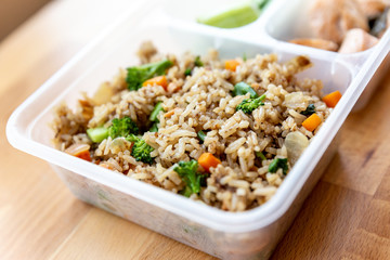 Organic fried salmon diced steak with onion, broccoli and carrot fried rice served with cucumber and lime in food grade box.