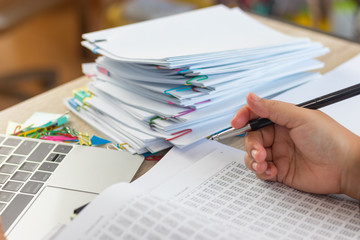 Hand of Asian business analyst holding pen is analyzing numbers of Statistics in office. Unfinished...