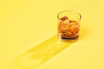 whiskey on the rocks with yellow background with sun streak