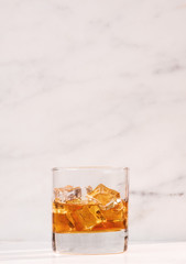 glass of whiskey or tea with ice on marble background vertical side view