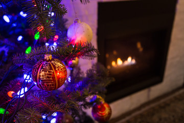 Close-up of bulbs hanging on a christmas tree with a fireplace in the background.
