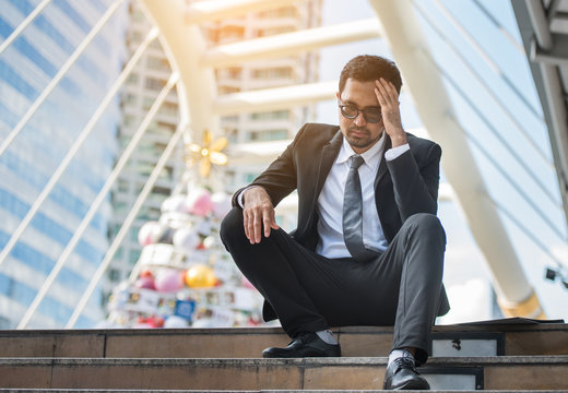 Stressed caucasian businessman sitting on steps in business area worrying about his future
