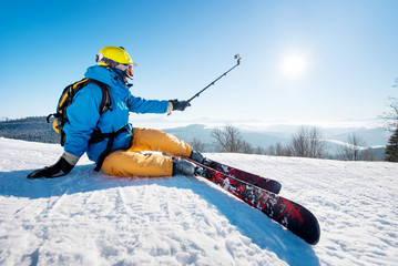 Shot of a skier sitting on the ski slope taking a selfie using selfie stick resting relaxing...