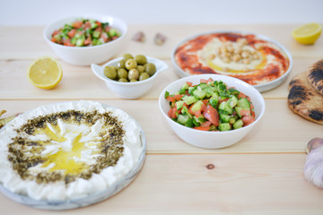 plates of Traditional homemade hummus with red paprika olive oil garlic and homemade labneh middle eastern soft white goat's milk cheese,arabic vegetable salad , pita bread on rustic table background 