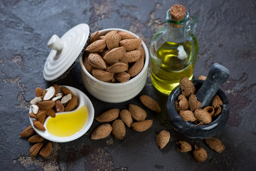 Unpeeled almond nuts and almond oil over brown stone background, horizontal shot