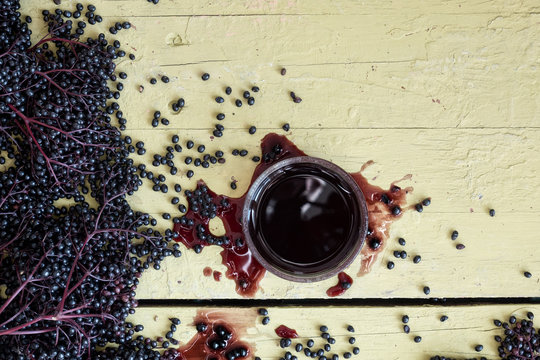 Frische reife violette schwarze Holunderbeeren gequetscht und gepresst und Holundersaft auf rustikalem gelbem Holzbretter Hintergrund 