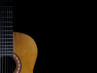 Part of a vintage, nylon string acoustic guitar body and neck are shown isolated, with solid black copyspace / text space to the right.