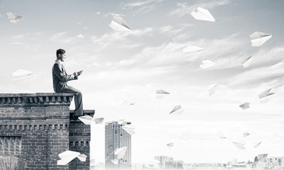 Businessman or student on roof edge making calls and cityscape a