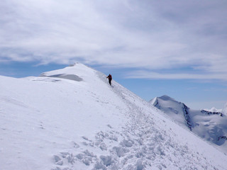 mountain climber hiking along a long snow ridge on his way to a high alpine summit with tracks in the foreground