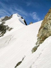 mountain climbers on a steep and narrow snow ridge leading to a high peak in the Swiss Alps