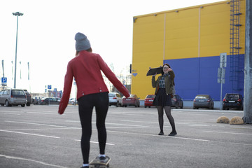 A young hipster girl is riding a skateboard. Girls girlfriends for a walk in the city with a skateboard. Spring sports on the street with a skateboard.