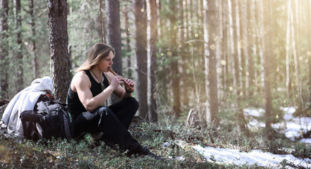 Fototapeta na wymiar A musician with a tool in nature. A man is playing a flute in a pine forest. The music of the druids in the spring forest.