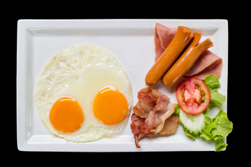 Top view of eggs and ham sausage with tomato on white plate, isolated on black