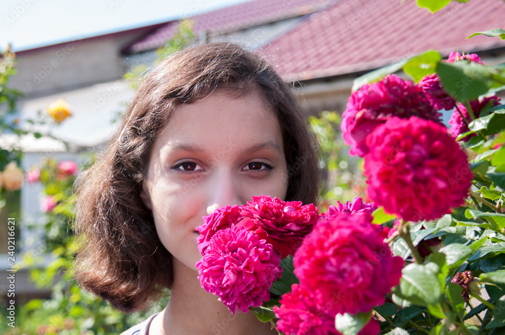 Wall mural portrait of a beautiful brunette in red rose bushes at summer cottage