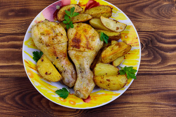 Baked chicken drumsticks with potatoes in a plate on wooden table