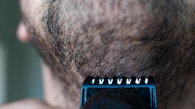 Close up man shaves beard on face with black razor. Unshaven man uses razor for shaving chin.