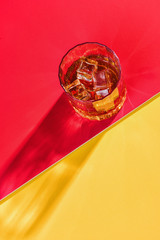 glass of whiskey and ice on red background top view