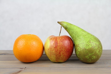 Owocowa dekoracja - pomarańcze, czerwone jabłko i zielona gruszka na jasnym tle
