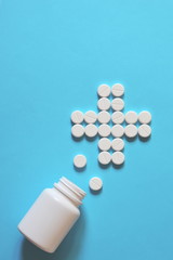 white pills laid out in the shape of a cross. white pills scattered on a blue background. pills spilled out of the bottle. copy space for text