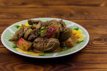 Stewed chicken liver with apple and onion on wooden table