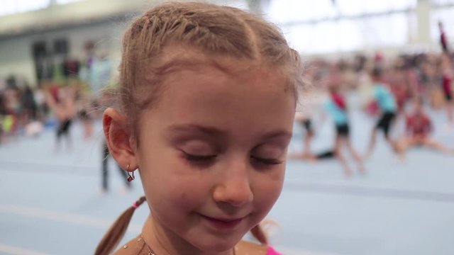 portrait of a little gymnast on the background of a large gym and gymnasts, cheerleading. competitions