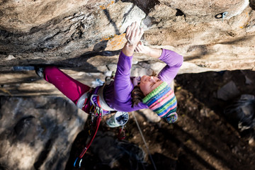 Girl rock climber climbs on the rock with the lower insurance men in colorful clothes and a hat in...