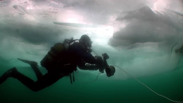 Diving under ice of cameraman underwater diver in cold water of lake Baikal.