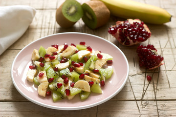 Salad of slices of various fruits and pomegranate seeds on a wooden background.