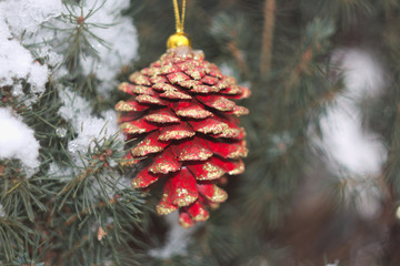 red Christmas pine cone with gold spangles on the background of snow-covered coniferous tree close-up