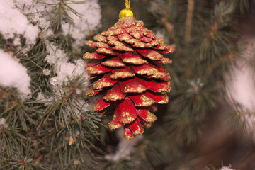 red Christmas pine cone with gold spangles on the background of snow-covered coniferous tree close-up