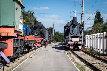Old steam locomotive beside a railway station platform. Retro train.