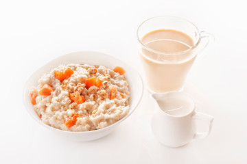 Fototapeta na wymiar Oatmeal with pumpkin and nuts in a plate, a glass of tea and a jug of milk on a white background. Close-up. Copy space