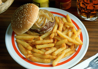 Plato combinado con un bocadillo de hamburguesa y cebolla a la plancha en un panecillo de semilla de sésamo y patatas fritas.