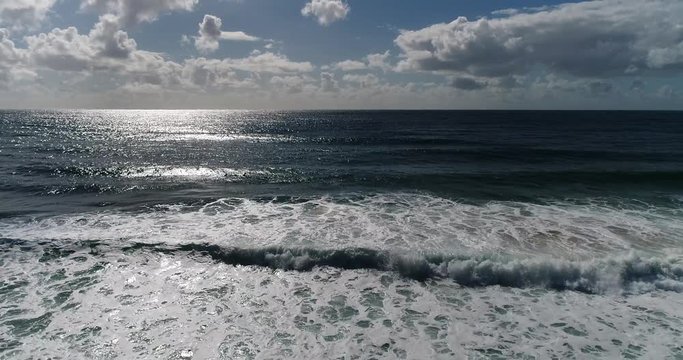 Off sandy Narrabeen beach facing rolling waves towards open sea horizon and hovering around wide panoramic landscape of Sydney Northern beaches.
