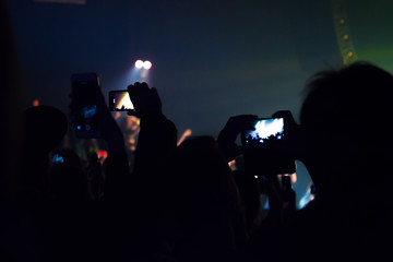 People watching a concert and someone shooting photo and video with a cellphone