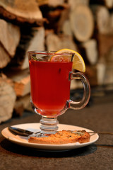 berry tea with lemon in a transparent glass on the background of wooden logs, Christmas tea