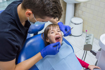 A male dentist is examining a child patient’s teeth
