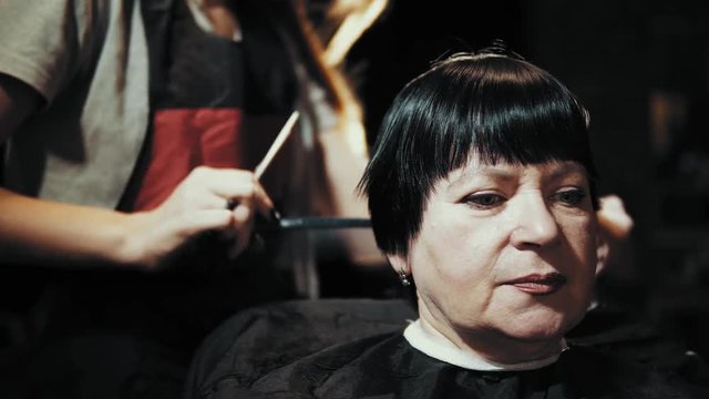 Mature Woman Having Her Hair Cut At The Hairdresser's. Closeup View Of A Hairdresser's Hands Cutting Female Dark Hair With A Thinning Shears In Beauty Salon.