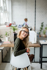 Portrait of a smiling young blond long-haired female student with blurred teachers and others in the classroom