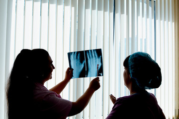 Female doctor and laboratory assistant look and discuss x-ray image and radiograph at hospital....