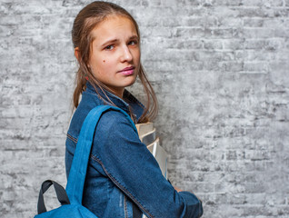 portrait of young teenager brunette girl with long hair holding books and note books wearing backpack on gray wall background