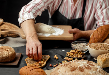 Close up of male baker hands kneading dough and making bread with a rolling pin on table with a freshly baked variety of bread loafs on foreground.