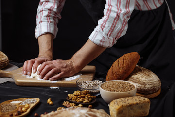 Hands of caucasian man prepares pastry by himself, close up. Man kneads dough on wooden counter with flour and rolling pin, baking organic bread or delicious bun.