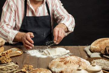 Hands of caucasian man prepares pastry by himself, close up. Man kneads dough on wooden counter with flour and rolling pin, baking organic bread or delicious bun.