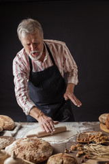 Friendly looking senior Chef Cook sheets dough with rolling pin indoor bakes delicious cakes or...