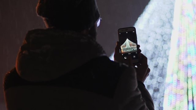 Rear view: Bearded man taking pictures of European Christmas market scene on smartphone