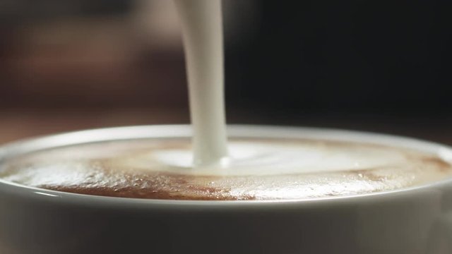 Slow motion closeup pour steamed milk into cappuccino