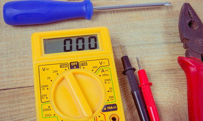 Electrical tester and other tools of electrician on a wooden background.